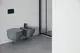 Wandhängendes, graues WC und Bidet von Ideal Standard, in minimalistischer Badausstattung, vor grauem Boden und heller Wand, mit gläserner Duschabtrennung im Hintergrund.